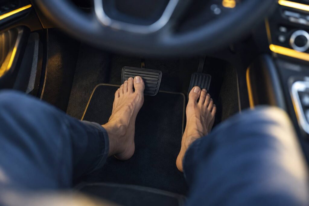 Vue large de l'intérieur d'une voiture moderne : pédales d'accélérateur et de frein vues en plongée, pieds nus